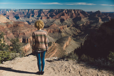 Rear view of woman standing on rock against sky