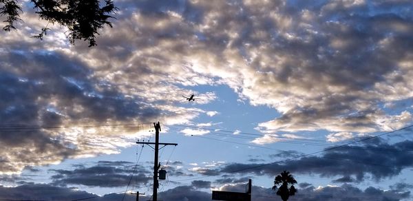 Low angle view of silhouette birds on cable against sky