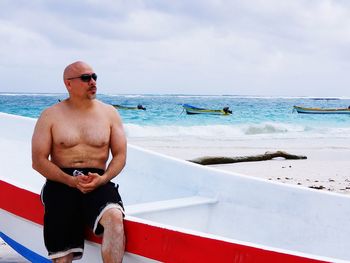 Man sitting on boat at beach against sky