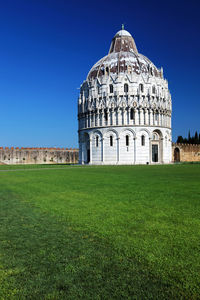 Grassy field by pisa baptistery against clear blue sky