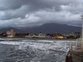 View of city at waterfront against cloudy sky