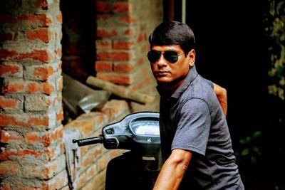 Man in sunglasses with motor scooter by brick wall