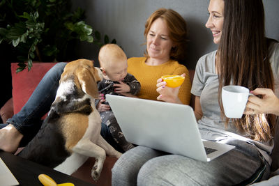 Happy family - grandmother, daughter, newborn baby and dog rest in the living room on the couch