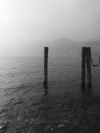 Wooden posts in sea against sky during foggy weather