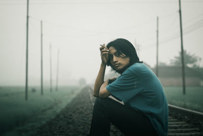 Man holding cigarette while sitting on railway track