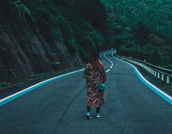 Rear view of young woman standing on road amidst trees