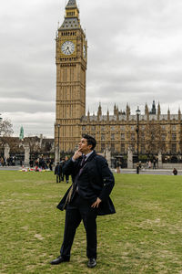 Man looking away while standing on grassy land against clock tower