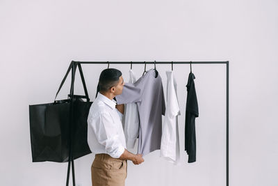 Young man choosing t-shirts from clothing rack at home