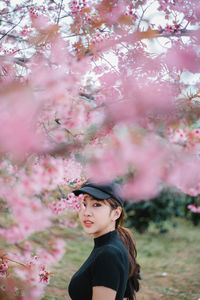 Side view of young woman standing by tree