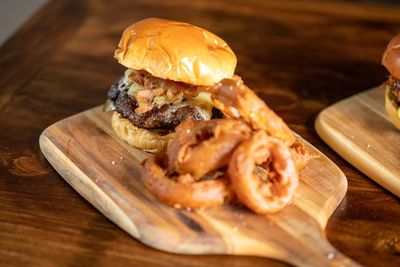 Cafe burgers and sliders with onion rings and other garnishes served on a wooden board.