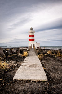 Lighthouse amidst sea and buildings against sky