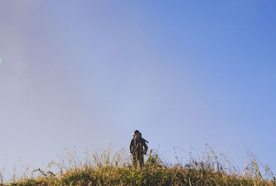 Low angle view of man standing on grassy hill against sky