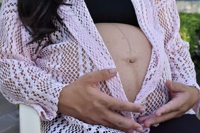 Midsection of pregnant woman touching stomach while sitting on chair