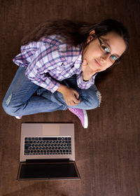 High angle portrait of girl sitting by laptop at home