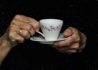 Close-up of hand holding coffee cup against black background