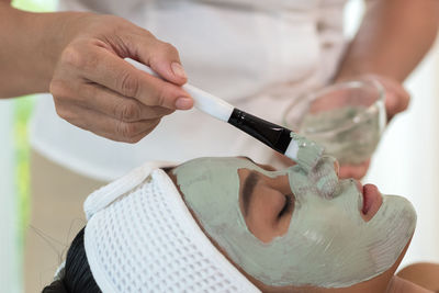 Midsection of beautician applying facial mask on woman face at spa