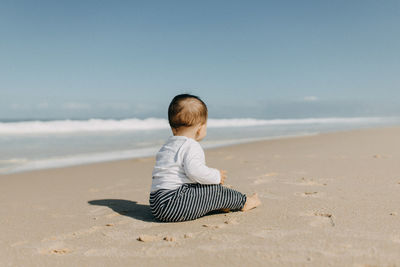 Rear view of boy sitting on beach against sky