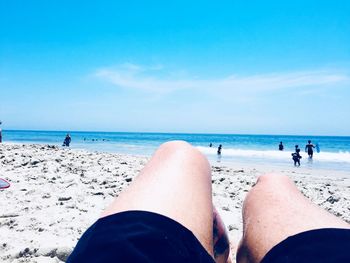 Low section of people on beach against sky