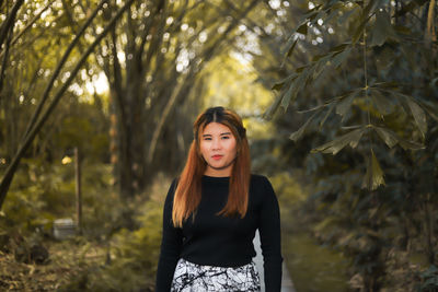 Portrait of young woman standing against trees