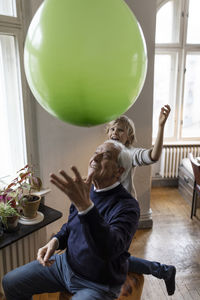 Happy grandfather and grandson playing with balloon at home