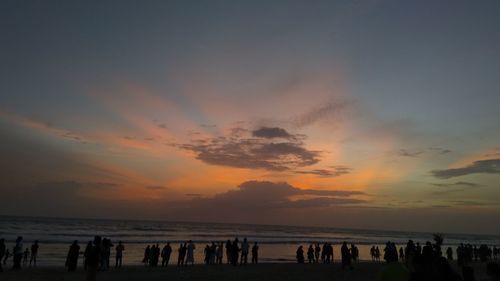 Silhouette people on beach against sky during sunset