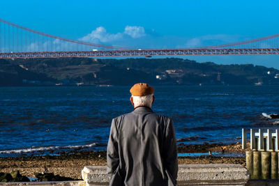 Rear view of man standing against bridge and sea
