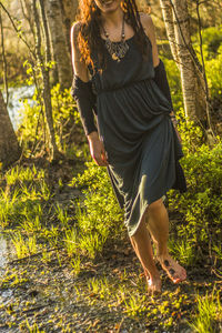 Low section of woman standing on grassy field in forest