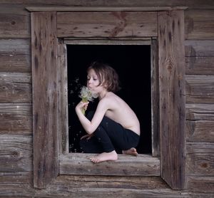 Woman looking away while sitting on wooden door