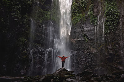 Woman standing on rock against waterfall in forest