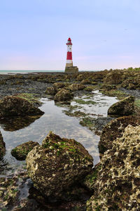 Lighthouse amidst rocks and buildings against sky