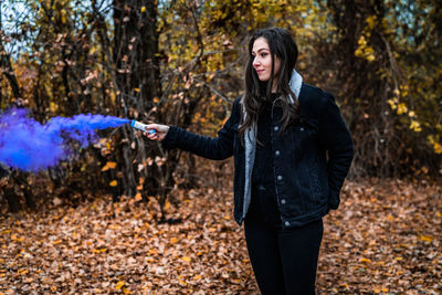 Young woman holding distress flare while standing in forest during autumn