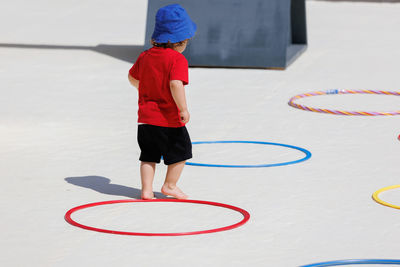 Small child in sun protective hat walking and playing between colorful circles placed on the ground.