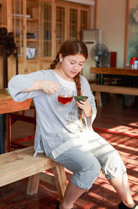 Girl making drink while sitting on wooden table at home