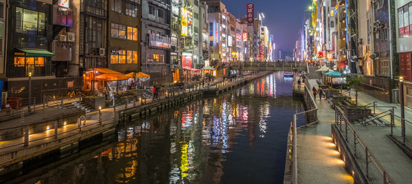 Illuminated street by buildings in city at night