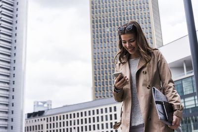 Young businesswoman walking in city using mobile phone