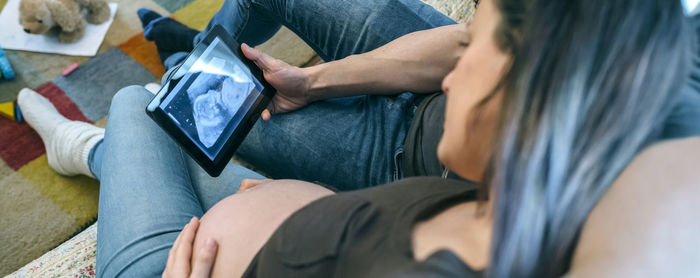 High angle view of couple using digital tablet while sitting on sofa at home