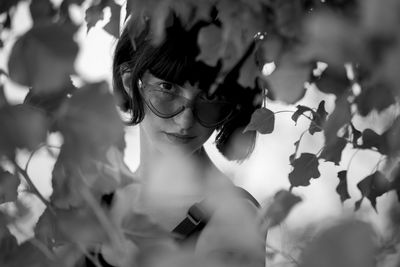 Close-up portrait of woman wearing sunglasses seen through leaves