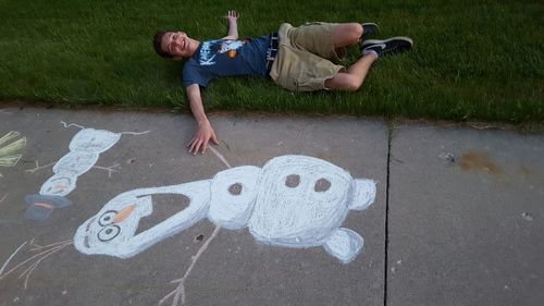 High angle view of young man lying on grassy field by drawing over road