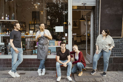 Multiracial shop owners talking to each other outside deli