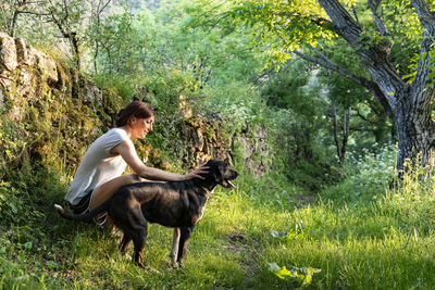 Woman petting and playing with her dog in a forest.