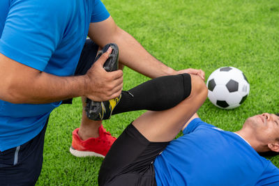 Low section of male physical therapist stretching soccer player leg on field