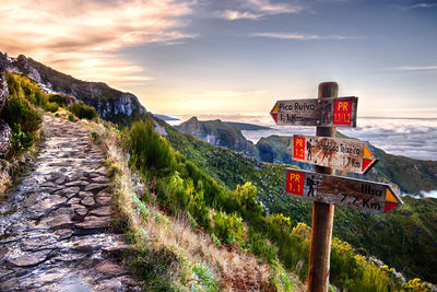 Road sign by mountains against sky during sunset