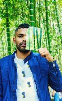 Portrait of man holding broken mirror against trees