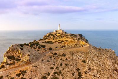 Lighthouse on rock by sea against sky