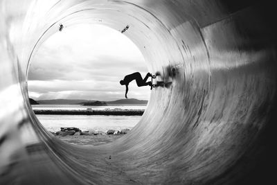 Silhouette man skateboarding in cement pipe at beach