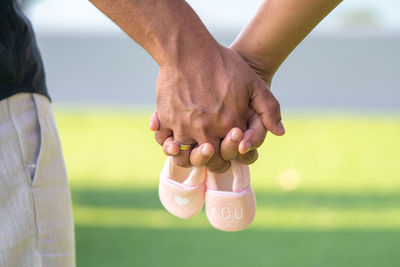 Cropped image of couple holding hands with baby booties against field