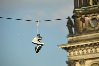Low angle view of shoes hanging from cable against clear sky