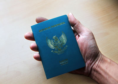 High angle view of hand holding passport with text over table