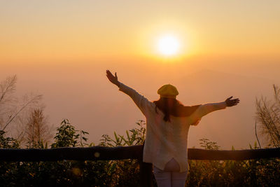 Rear view of woman with arms outstretched standing at sunset