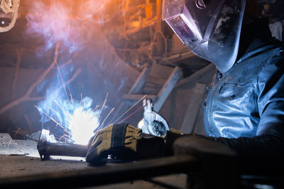 Welder in a workshop welds a metal part. general plan of an old cluttered garage where a man in